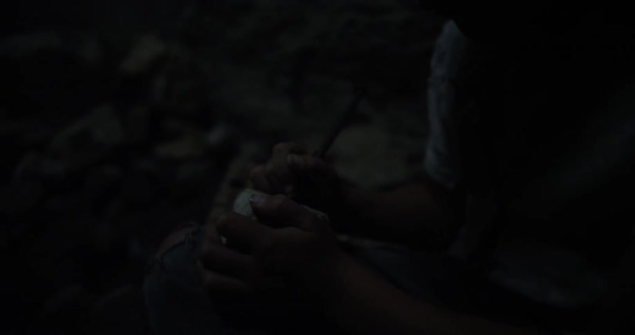 A boy writes on a rock with a stick