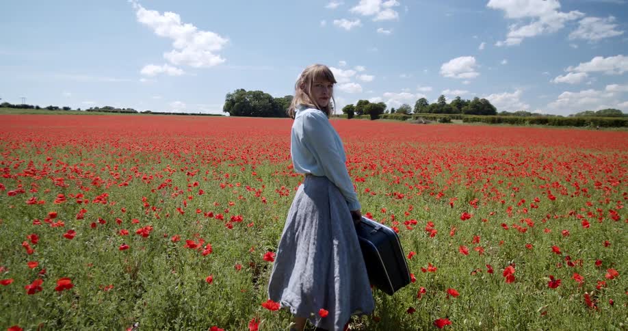 Woman holding a suitcase twirls from side to side as she stands in a floral field