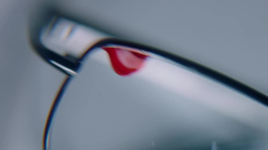 A glasses with some blood on the lens with a white background