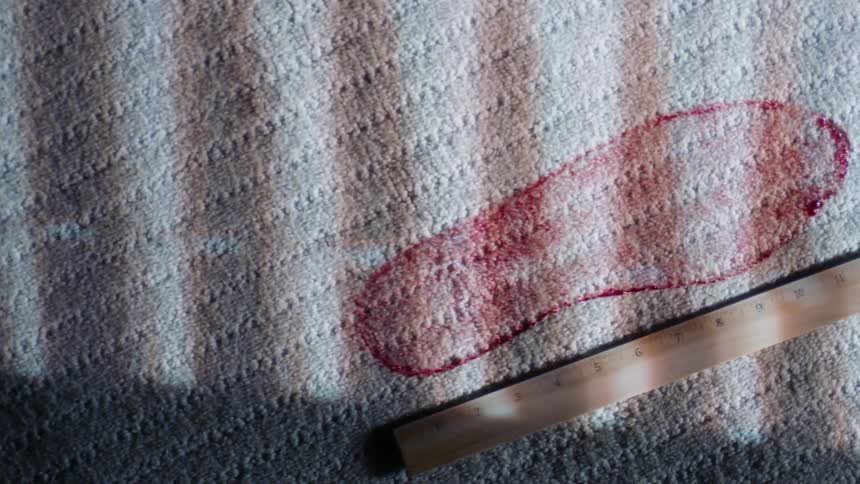 A bloody shoe print on a rug next to a ruler