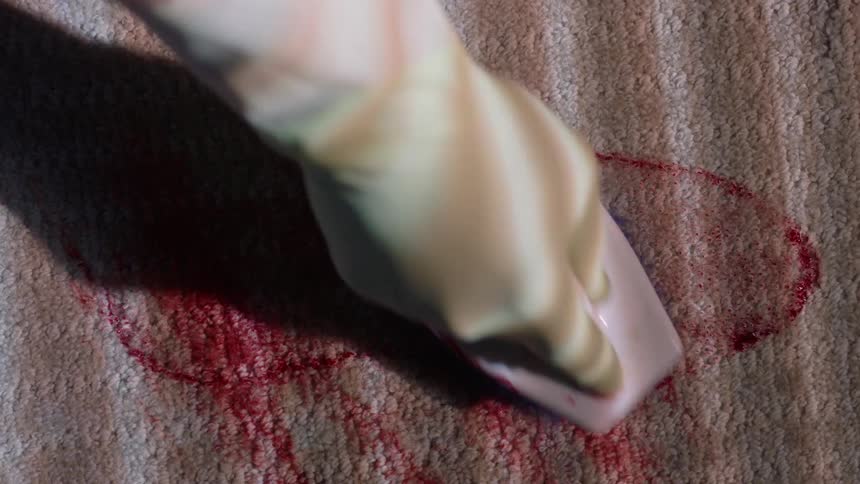 A gloved hand scrubs a bloody footprint on carpet