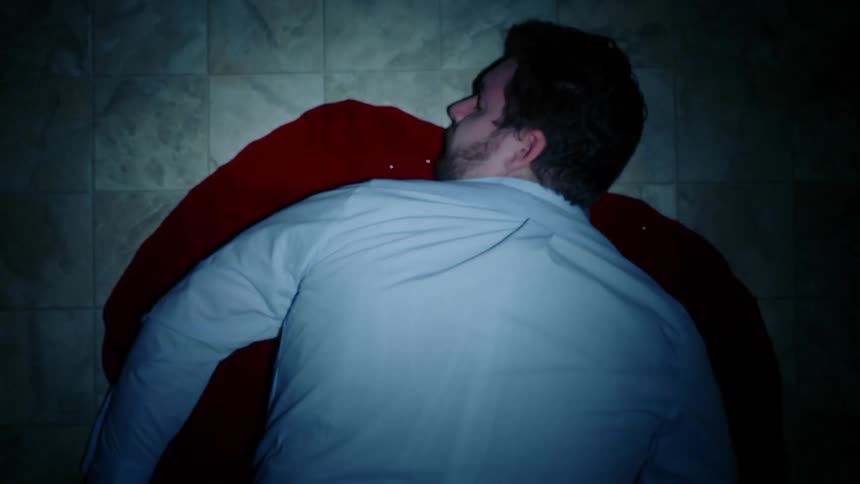 The corpse of man lying in a pool of blood on a tiled floor in a dimly lit room