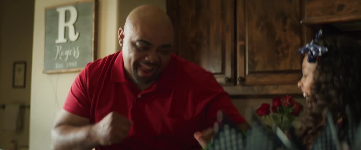 A young girl throws something in her dads mouth and they laugh and fist bump after