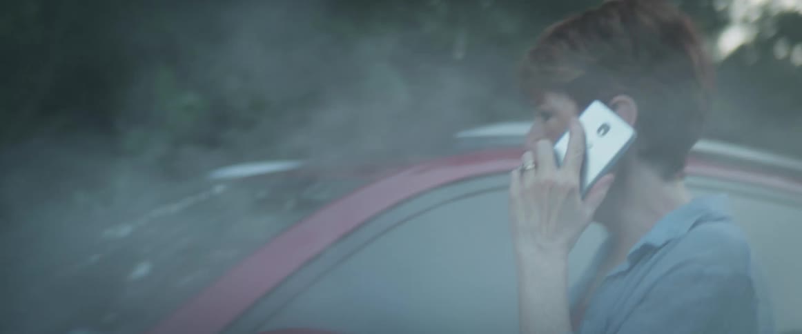 A woman talks angrily on her phone as she walks around her smoking vehicle