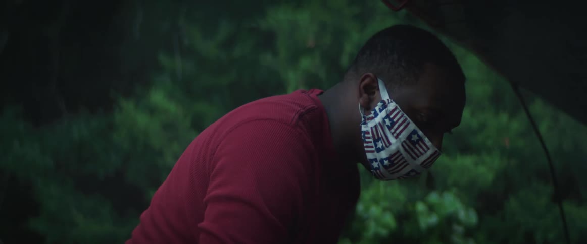 Man wearing a face mask helps to repair a womans car that broke on the side of the road