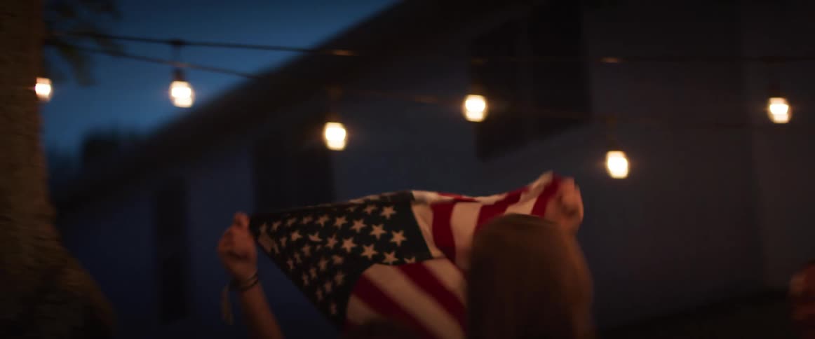 A group of friends talk in a back yard as one boy runs past them with a flag