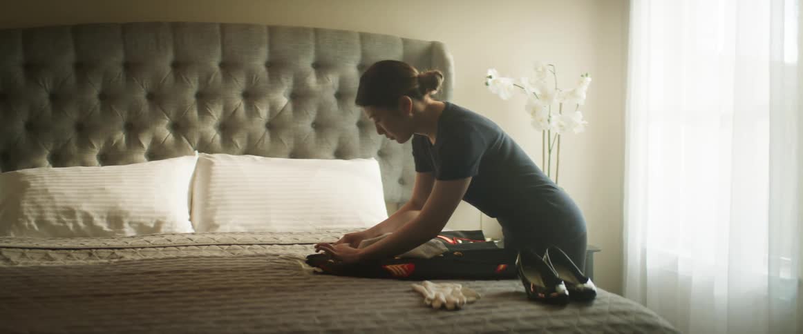 An Asian woman spot cleans a uniform on a bed and then carries it away satisfied