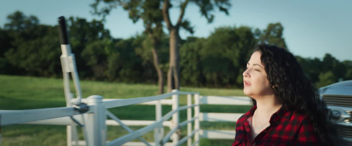 A woman gets out of a truck and walks over to a fence and looks out at the farmland