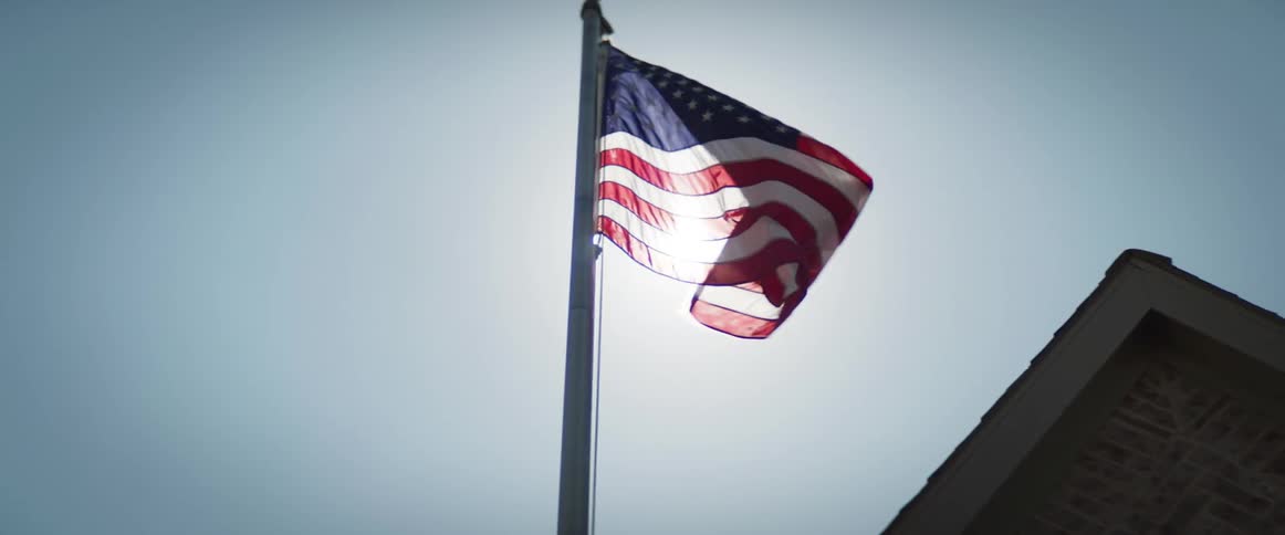 The american flag attached to a pole flutters in the wind under the sun