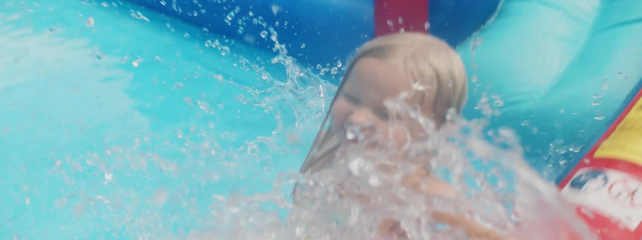 A little girl slides down an inflatable water slide into a small pool at the bottom