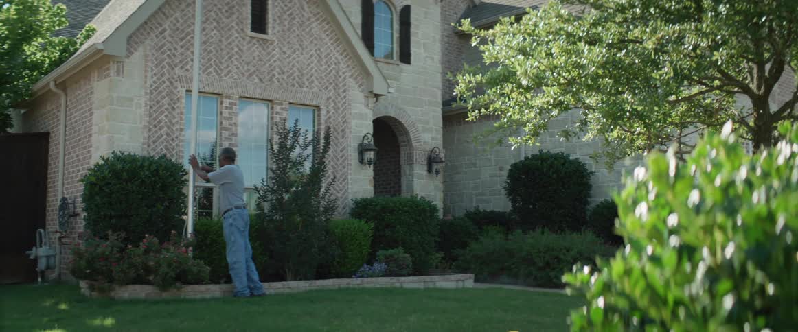 A man raises an american flag up a flag pole in the front yard of his house