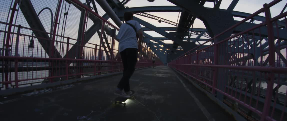 A person rides a lighted skateboard over a high pedestrian bridge