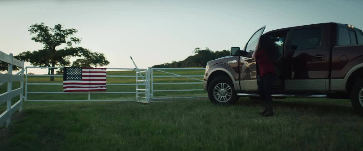 A woman drives up to the gate at a farm and gets out of her truck and looks over the landscape