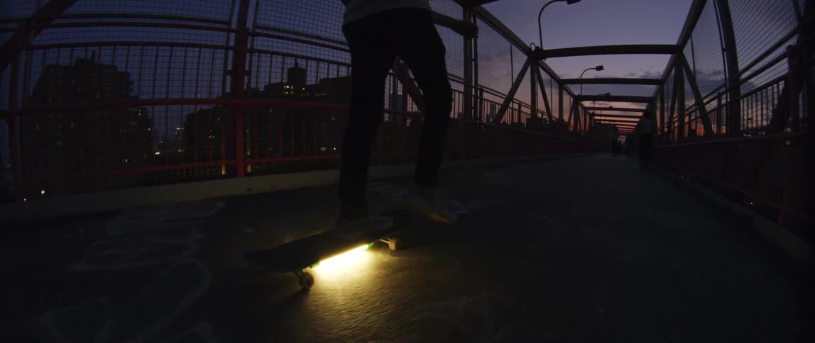 A man is skateboarding on a bridge in a downtown city at night