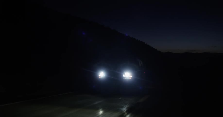 A vehicle drives down a road in the mountains at night