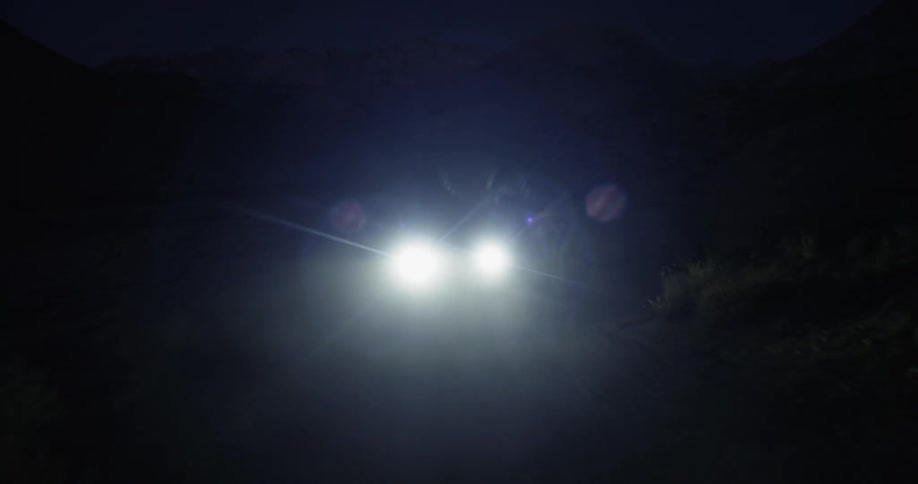 A vehicle driving on a dirt road with its lights on