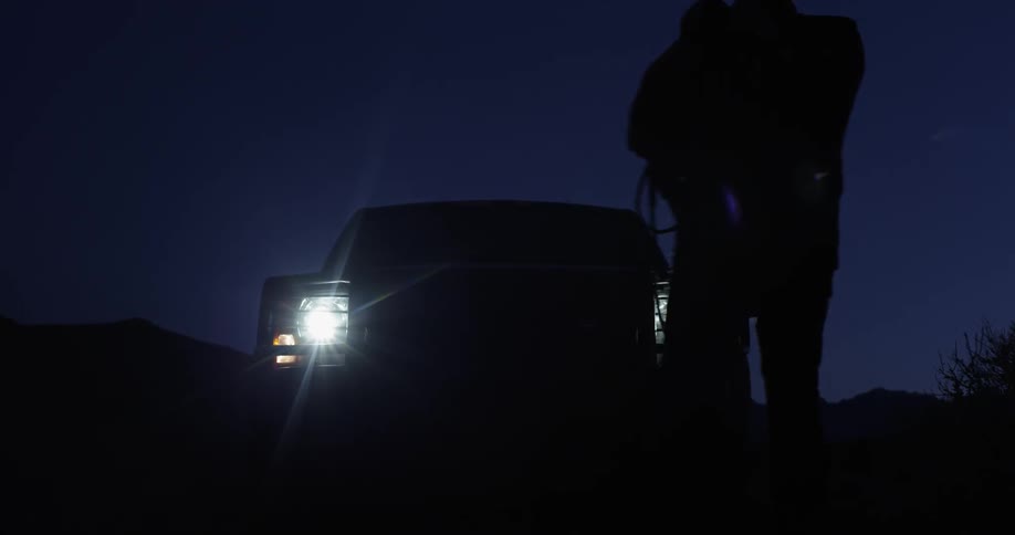 The headlights of a vehicle shine at night as a person walks in front of them
