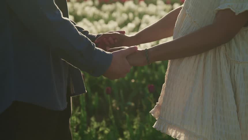 A man and woman in a field of flowers face one another and hold hands