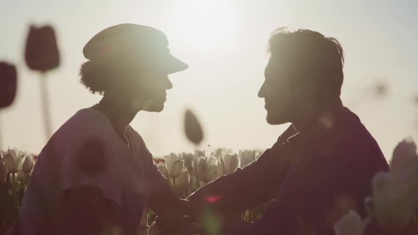 A man and a woman sitting in a field of flowers with the sky in the background