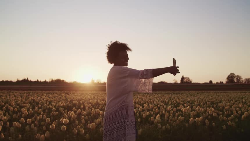 A young woman takes a selfie while standing in a field of yellow flowers