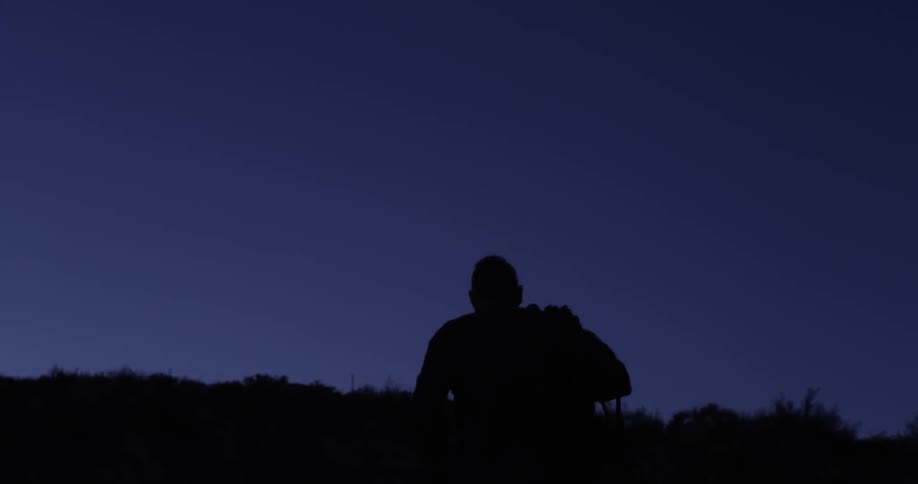 A man carrying rope over his shoulder as he walks towards a hill at dusk