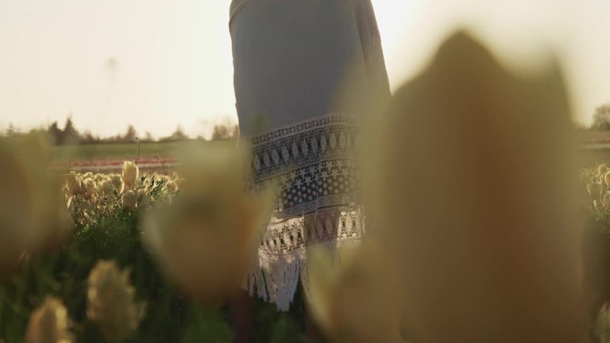 Young woman standing in a field of yellow tulips at sunset