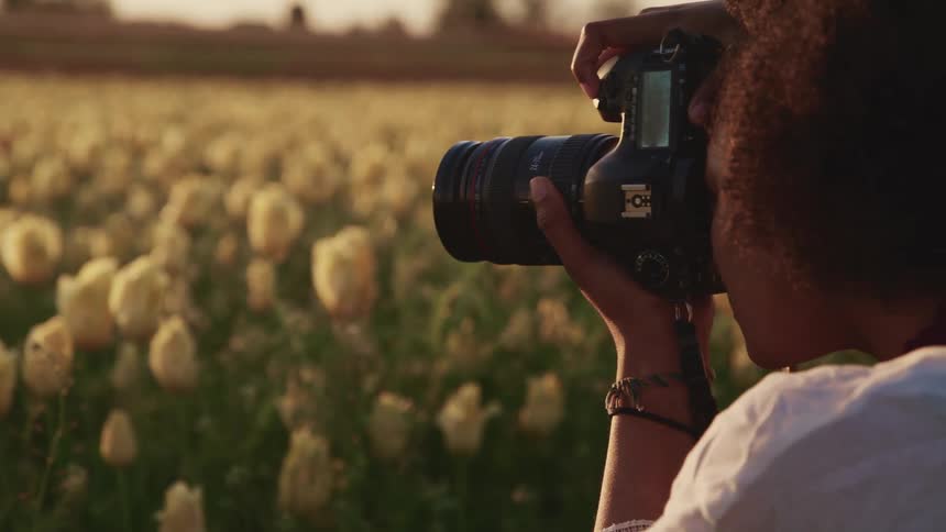 A female photographer uses a camera to take a photograph of a field of white flowers
