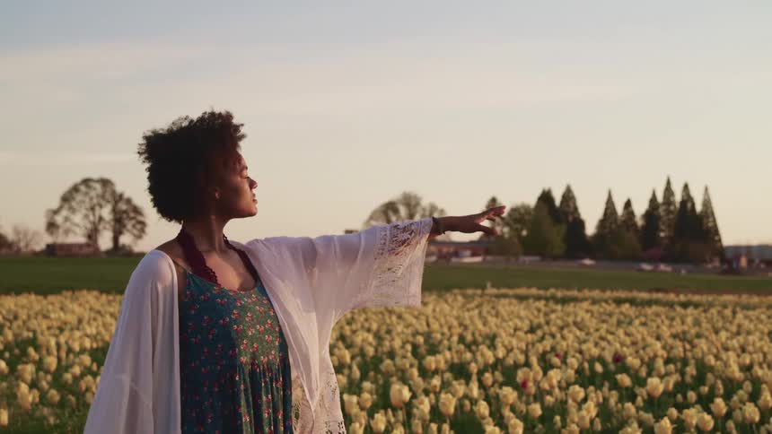 A woman raises her arm while standing in a field of flowers
