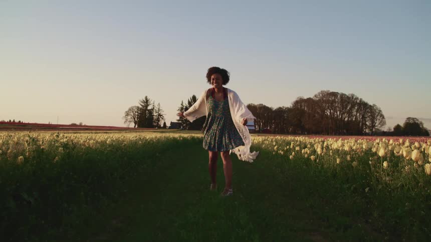 Young woman prances on a path between the tulip fields at sunset