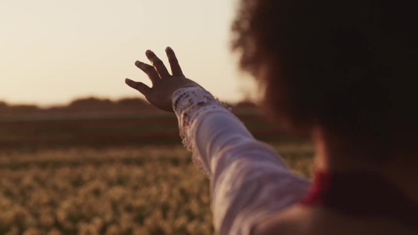 A woman standing in a field of flowers stretches her arm out to the side