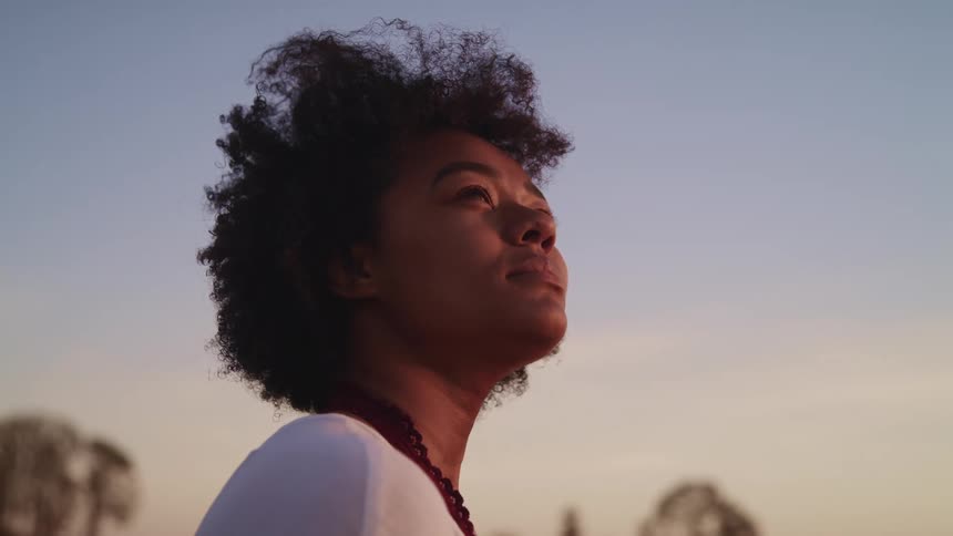 A woman looks at the sky while standing outdoors in the evening