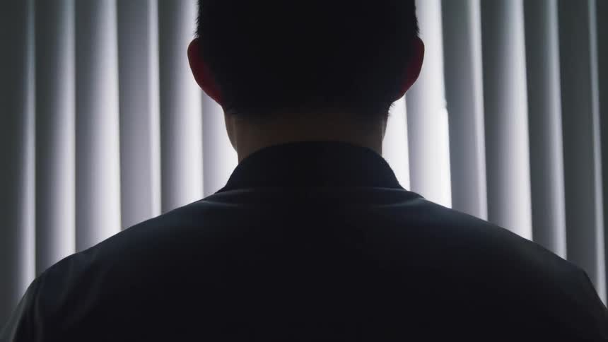 A man stands in front of a window in a hospital room as the blinds shake rapidly