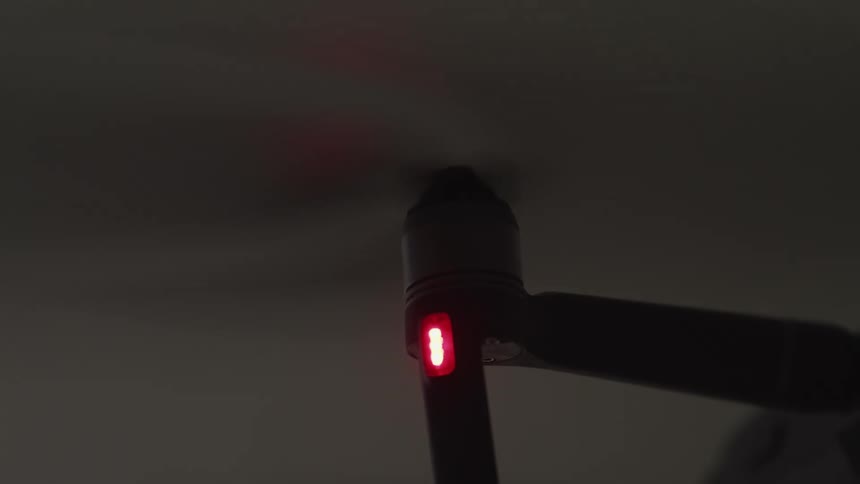 A propeller turning with a red light underneath it with the sky and clouds in the background
