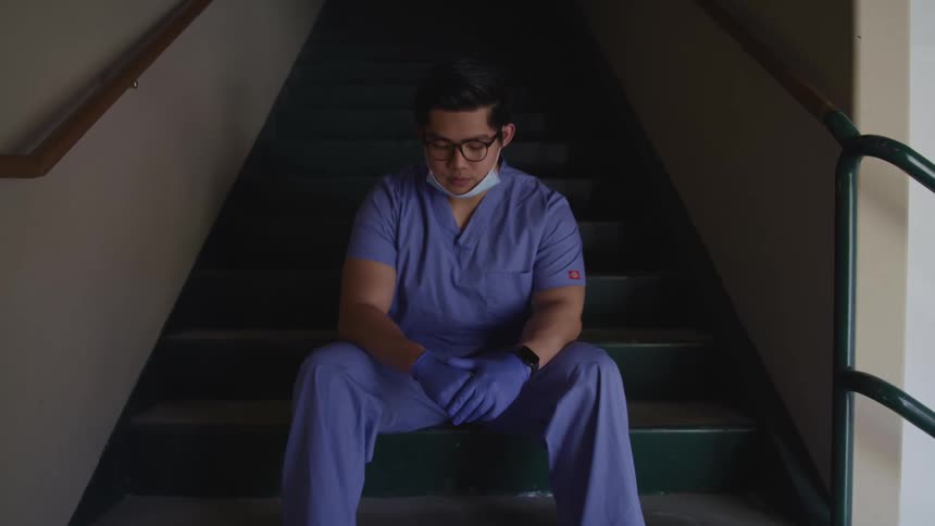 A doctor sitting in a stairwell looking sad