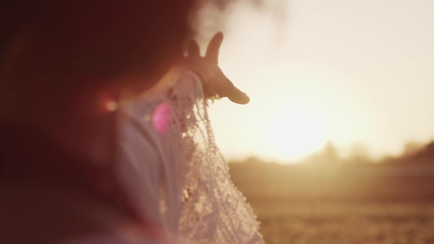 Young woman stands in a tulip field with hand extended to the setting sun