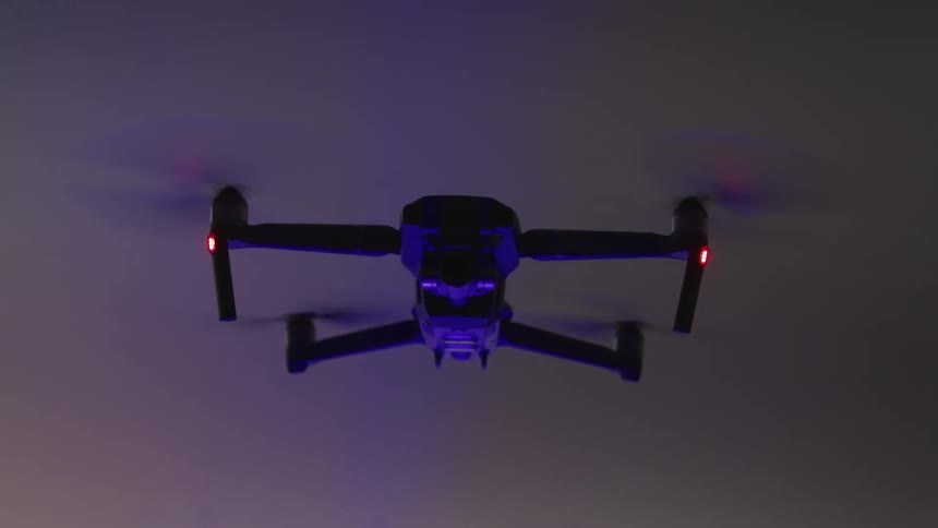 Drone with blinking blue and red lights hovers against grey background