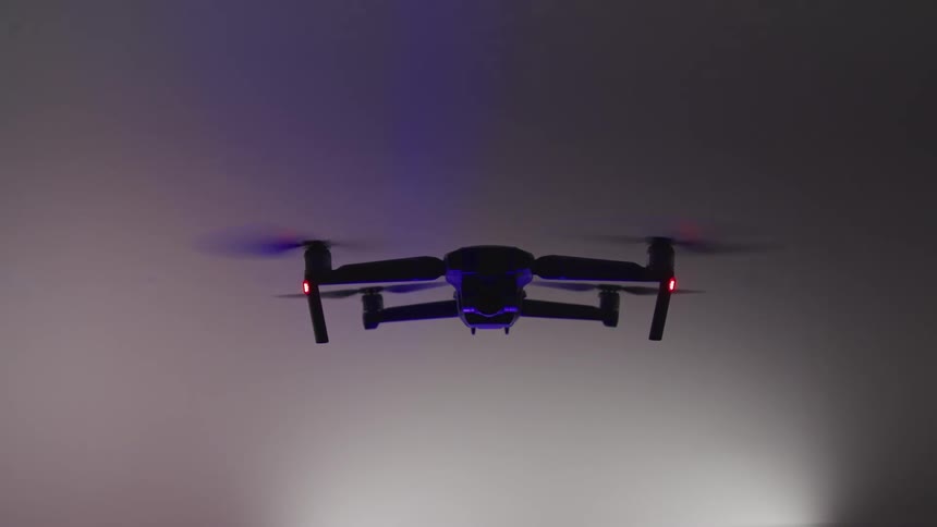 A drone with propellers hovering with a white and gray background