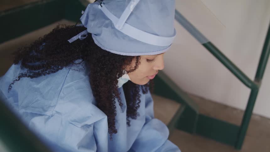 A nurse sitting in a stairwell drops her head to her chest