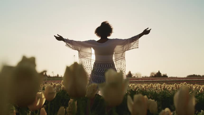 A woman raises her arms standing in a field full of flowers