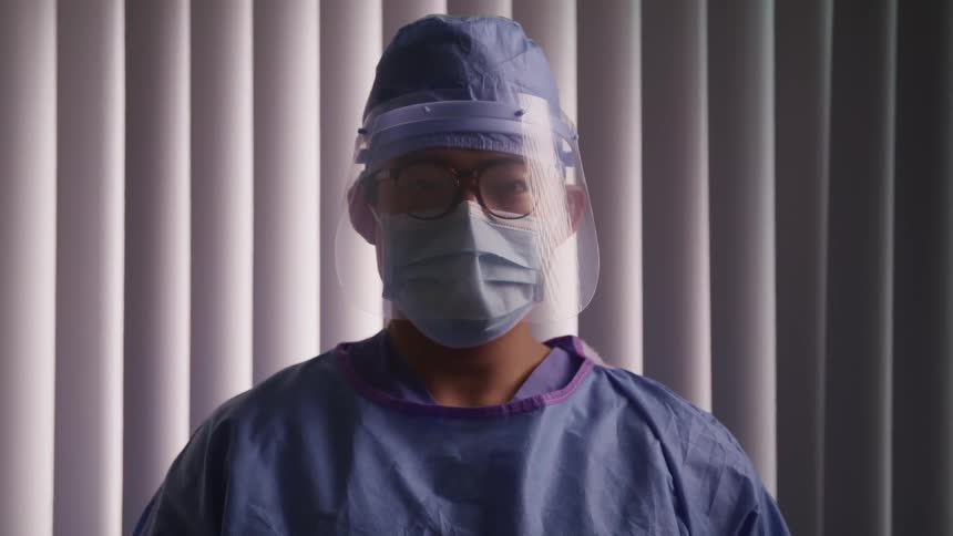 Young doctor wearing scrubs and protective gear looks at the camera
