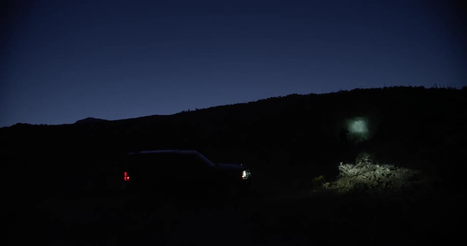 A person with a flashlight walks away from a vehicle at night