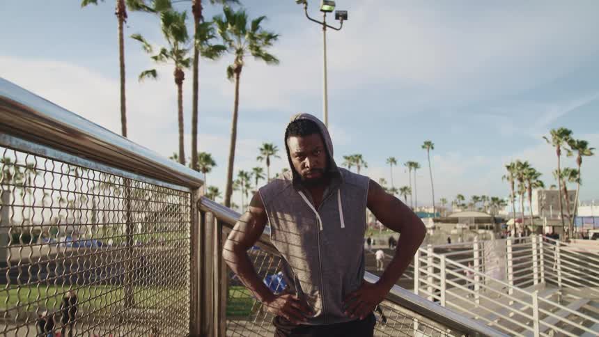 A man takes a break from working out and stands on an outdoor staircase at a park with his hands on his hips