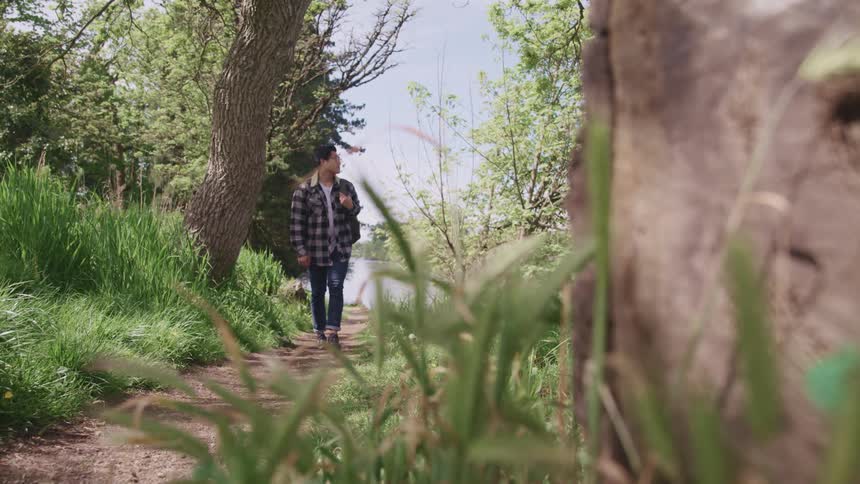 A teenager walks along a path in a wooded area and looks around