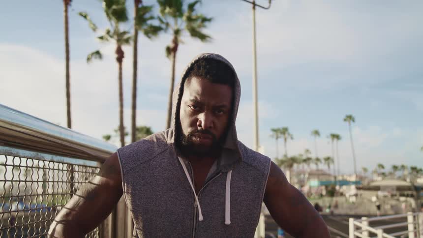 Muscular man wearing a sleeveless hoodie looks at the camera at sunset