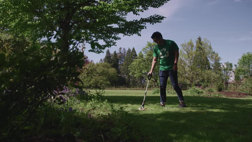 A man is picking up litter with a grabber in the woods