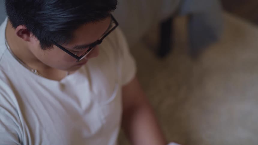Asian man with glasses and a white t shirt reads a book