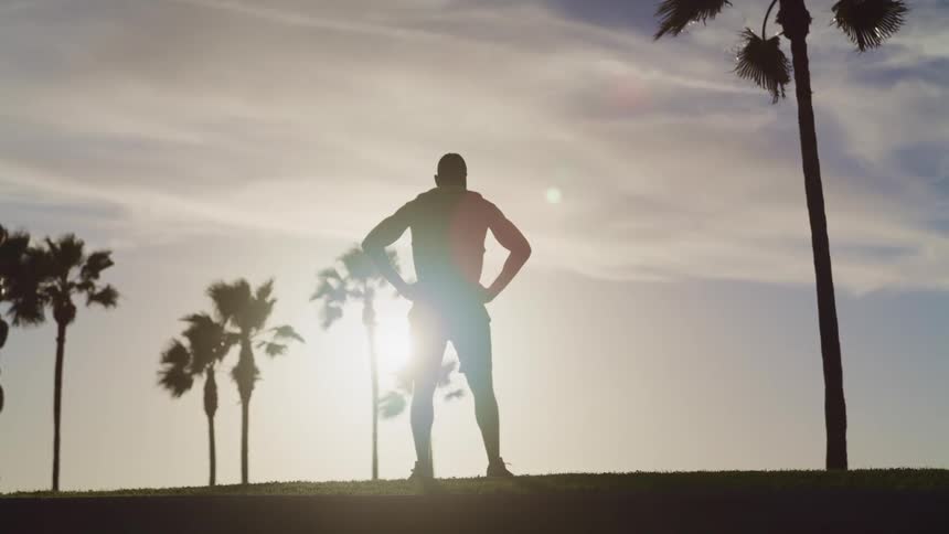 Silhouette of a strong muscular man standing with hands on his hips at sunset