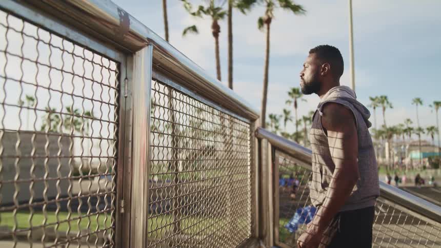 A man looks out over a metal fence on a sunny day