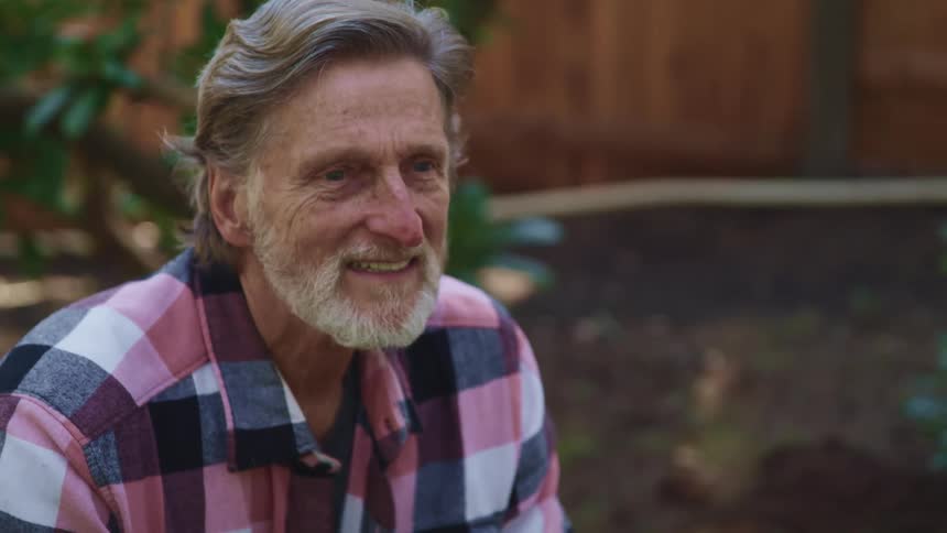 A man is sitting in the yard smiling