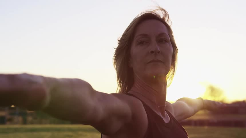 Elderly woman with dirty blonde hair spreads her arms wide at sunset
